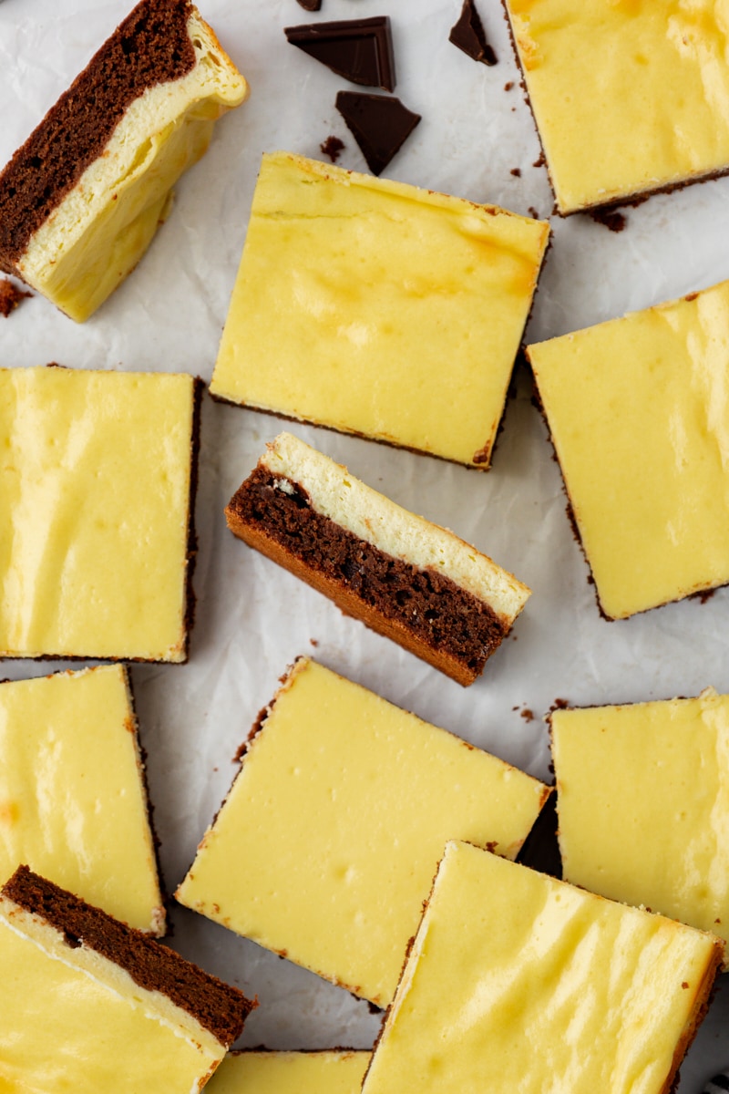 Overhead view of cheesecake brownies on parchment paper, with 2 brownies on their side to show layers