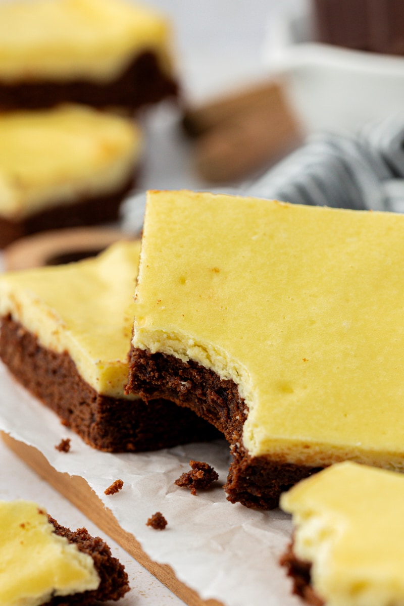 2 cheesecake brownies stacked on parchment paper, one with bite taken out