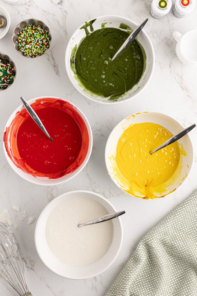 overhead view of bowls of green, yellow, white, and red royal icing