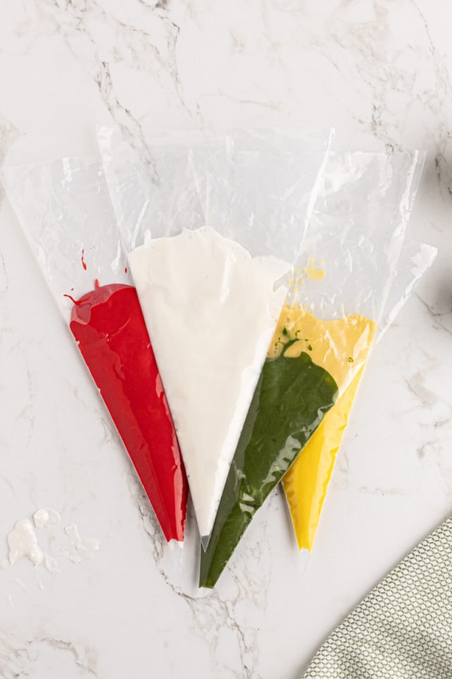 overhead view of piping bags filled with red, white, green, and yellow royal icing
