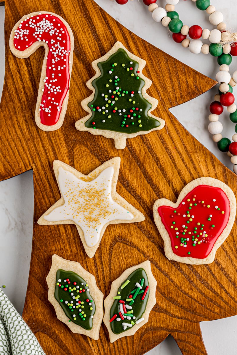 six cut-out sugar cookies decorated for Christmas and served on a tree-shaped wooden board