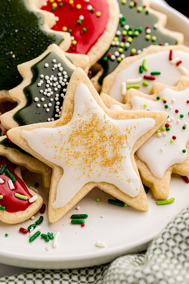 several cut-out sugar cookies in various Christmas-themed shapes on a white plate