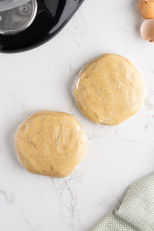 overhead view of two disks of cut-out sugar cookie dough wrapped in plastic wrap