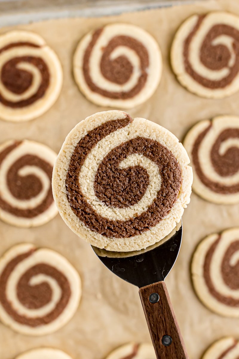 overhead view of a pinwheel cookie on a cookie spatula with more cookies on parchment paper in the background
