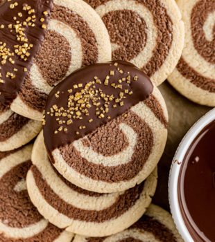 overhead view of pinwheel cookies on parchment paper with bowls of melted chocolate and gold sprinkles