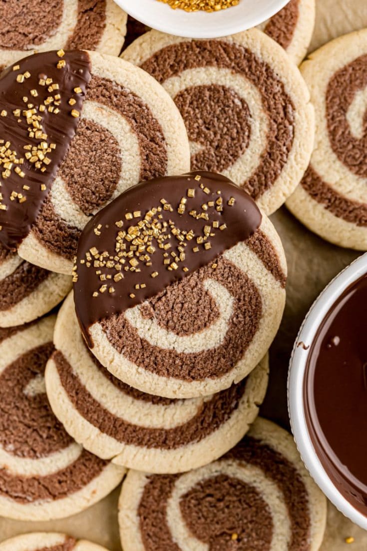 overhead view of pinwheel cookies on parchment paper with bowls of melted chocolate and gold sprinkles