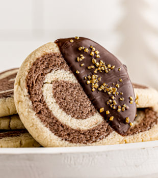 a chocolate-dipped pinwheel cookie propped against several other cookies on a white cake stand