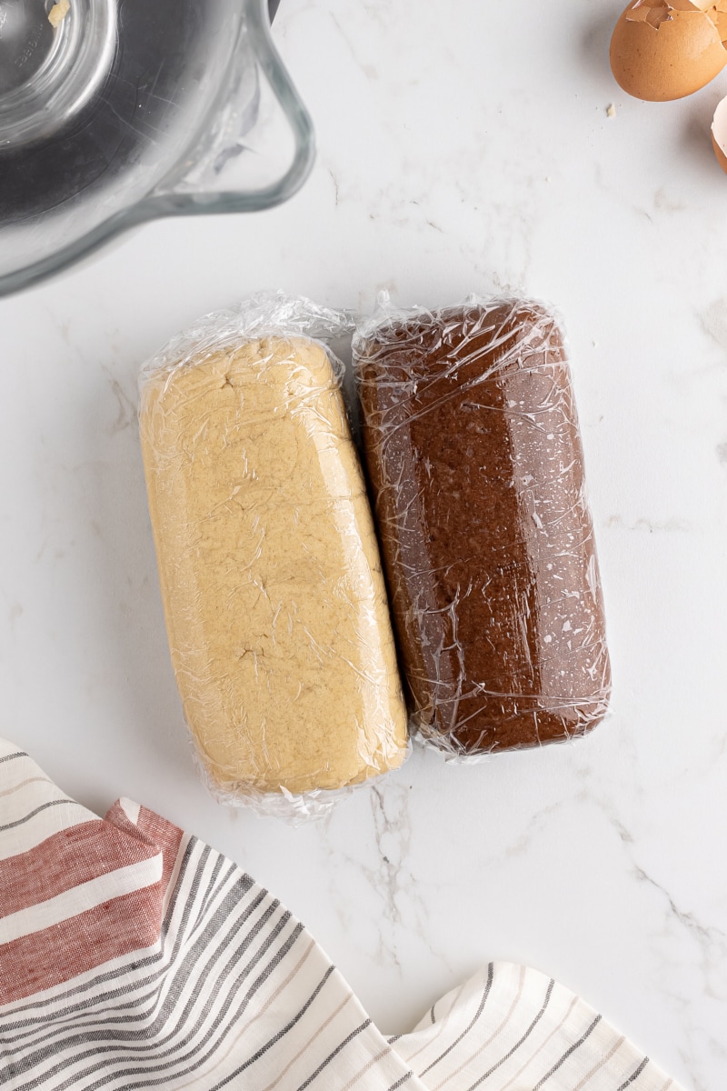 overhead view of vanilla and chocolate cookie doughs shaped into thick rectangles and wrapped in plastic wrap