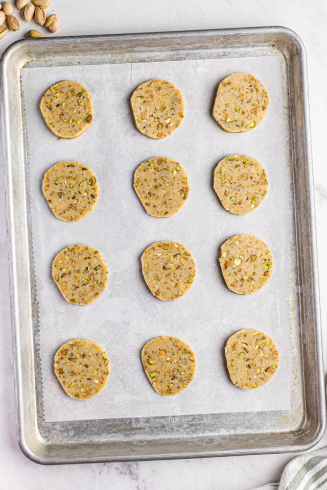 overhead view of sliced pistachio cookie dough on a parchment-lined baking sheet