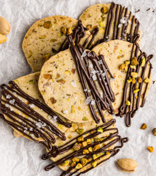 overhead view of a pile of chocolate-drizzled pistachio cookies on parchment paper