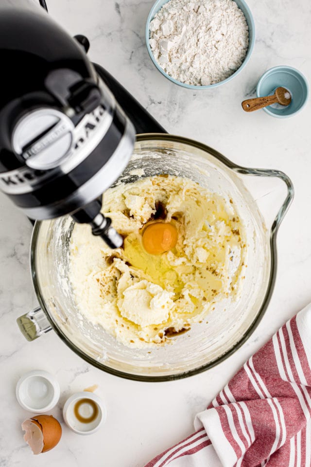 overhead view of egg, vanilla extract, and almond extract added to creamed butter and sugar in the bowl of a stand mixer