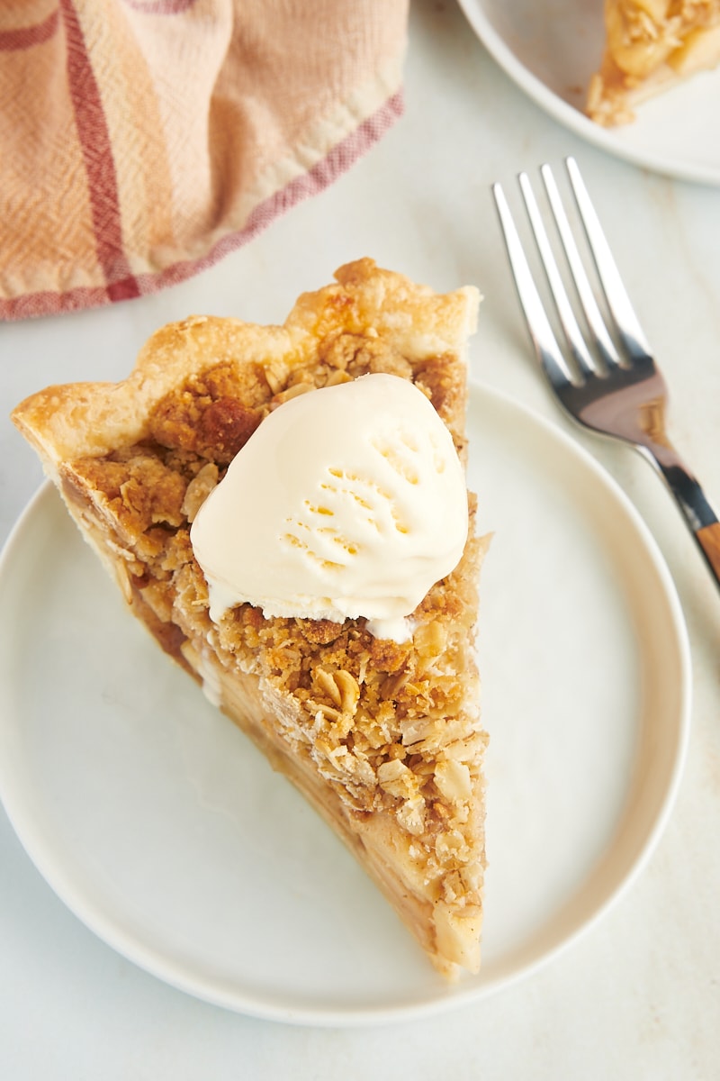 a slice of apple crumb pie topped with ice cream and served on a white plate
