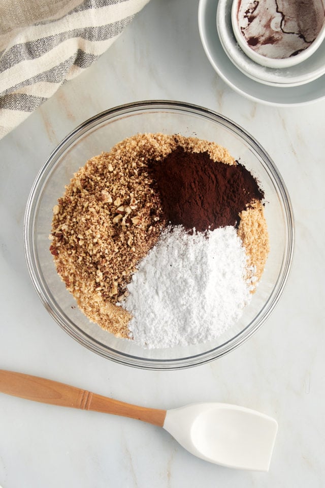 overhead view of vanilla wafer crumbs, chopped pecans, confectioners' sugar, and cocoa powder in a glass mixing bowl