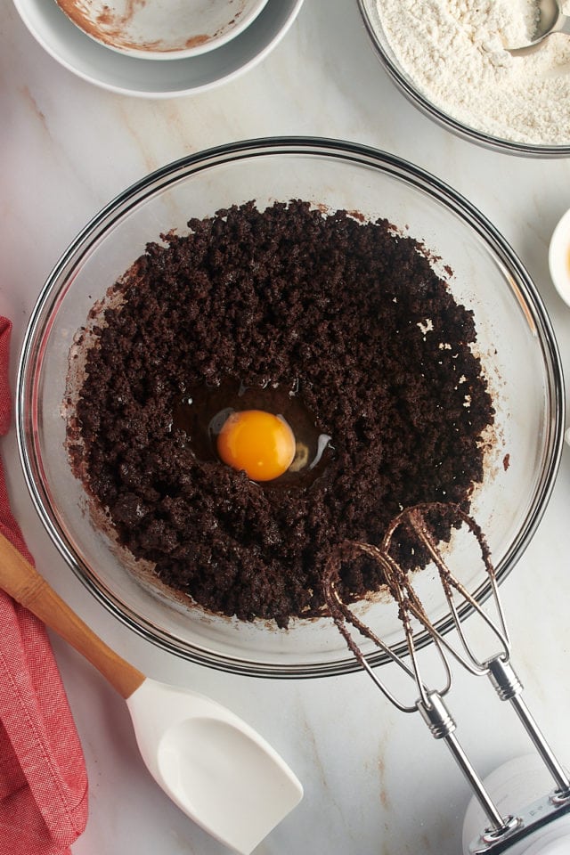 Overhead view of an egg added to partially mixed chocolate crinkle cookie dough.