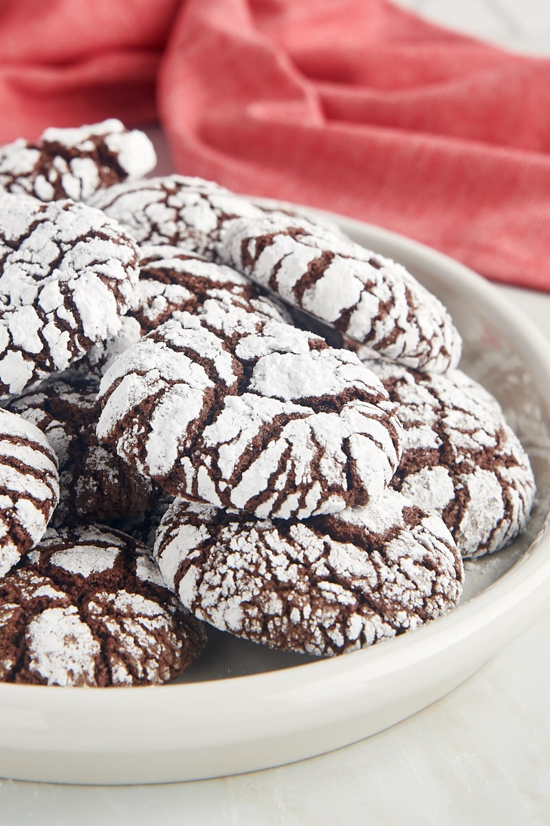 Chocolate crinkle cookies piled on a white plate.
