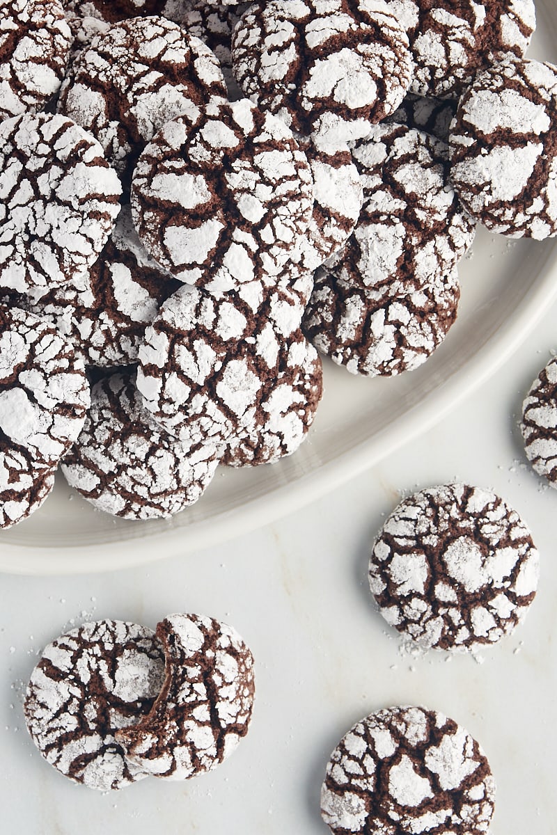Overhead view of chocolate crinkle cookies on a large white plate and on a marble countertop.