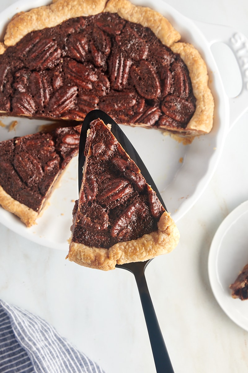 overhead view of a slice of chocolate pecan pie on a pie server over the remaining pie