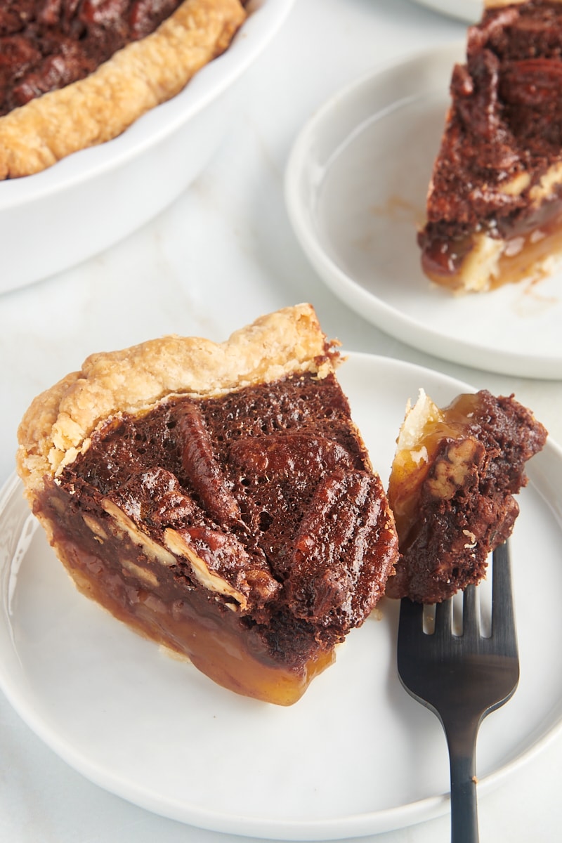 a slice of chocolate pecan pie on a white plate with a bite of pie on a fork