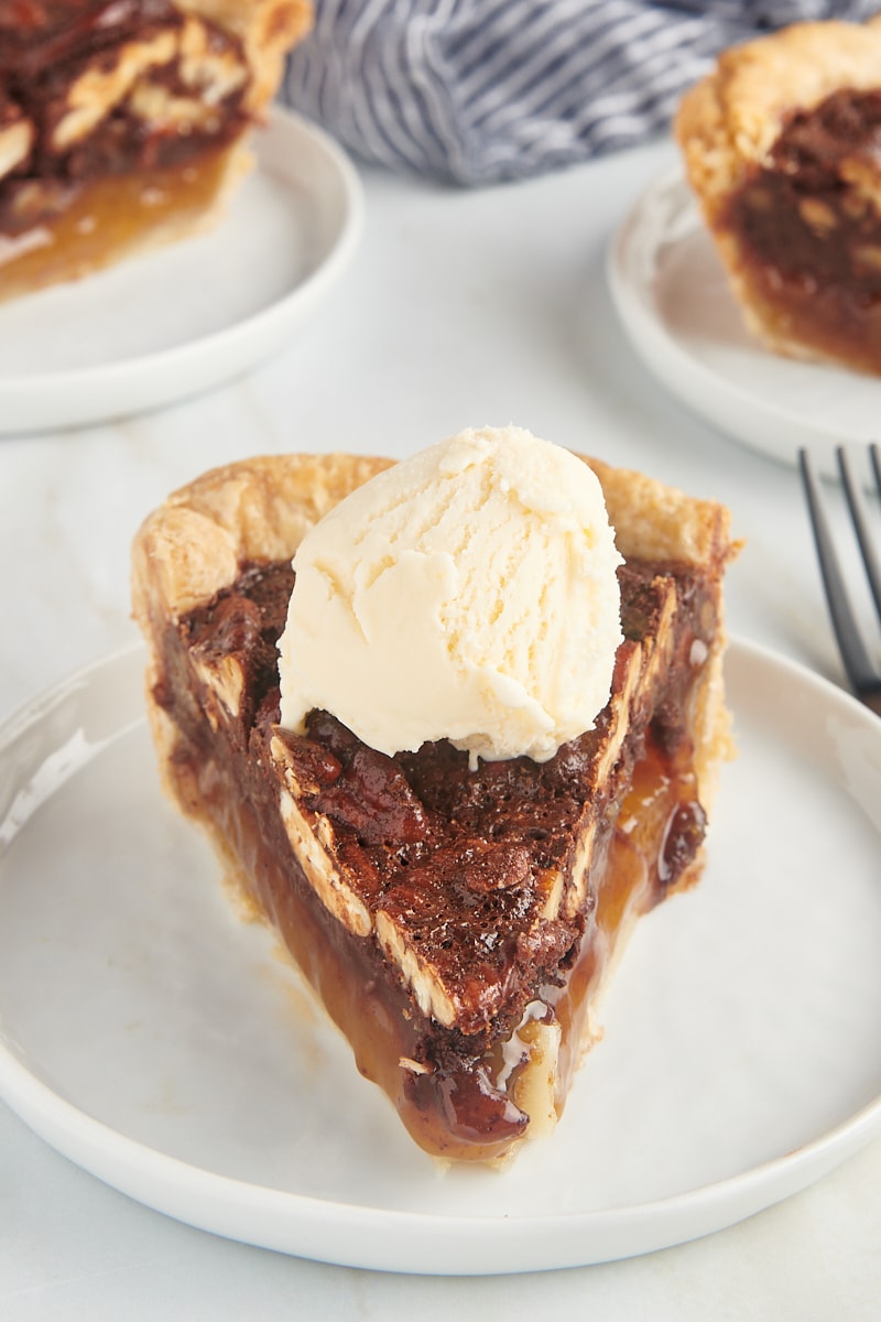 a slice of chocolate pecan pie topped with ice cream and served on a white plate
