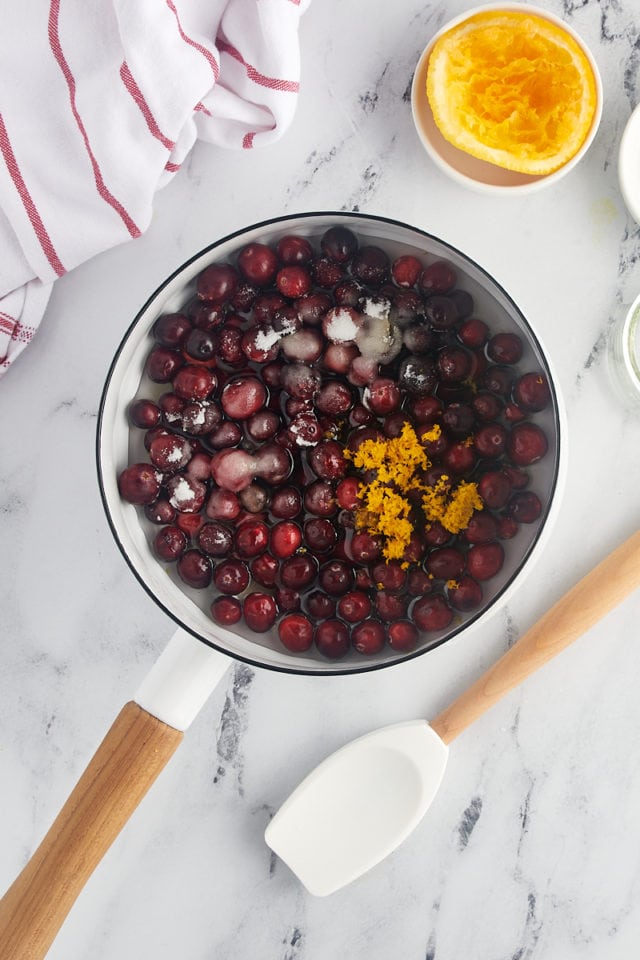 overhead view of cranberries, sugar, orange zest, orange juice, and water in a saucepan