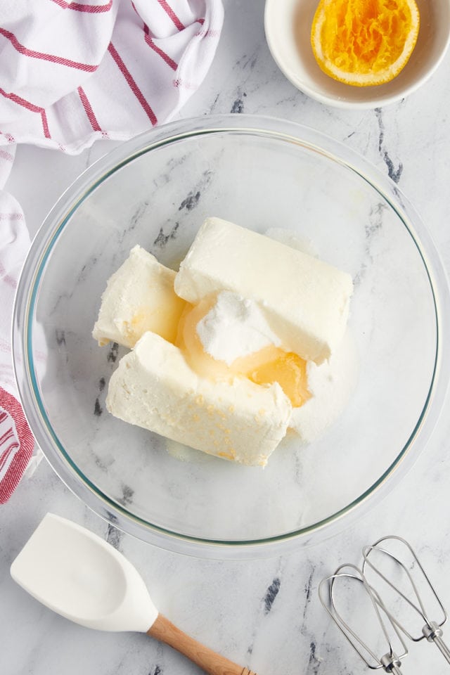 overhead view of cream cheese, sugar, and orange juice in a glass mixing bowl