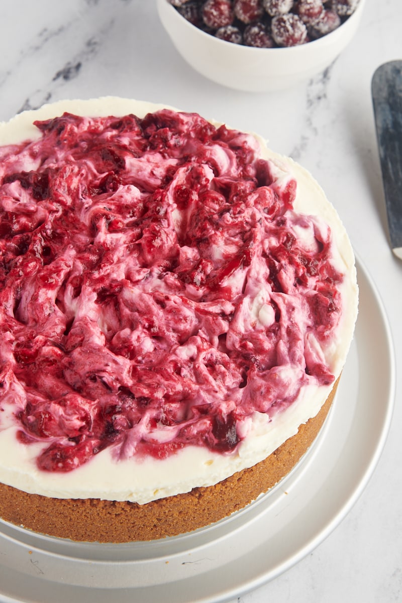 no-bake cranberry cheesecake on a metal serving plate with sugared cranberries in the background