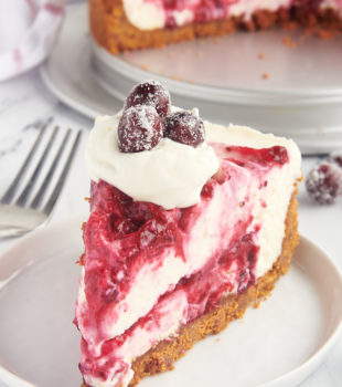 a slice of no-bake cranberry cheesecake topped with whipped cream and sugared cranberries and served on a white plate
