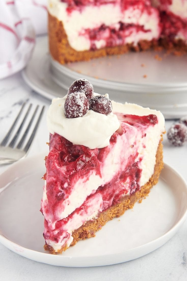 a slice of no-bake cranberry cheesecake topped with whipped cream and sugared cranberries and served on a white plate