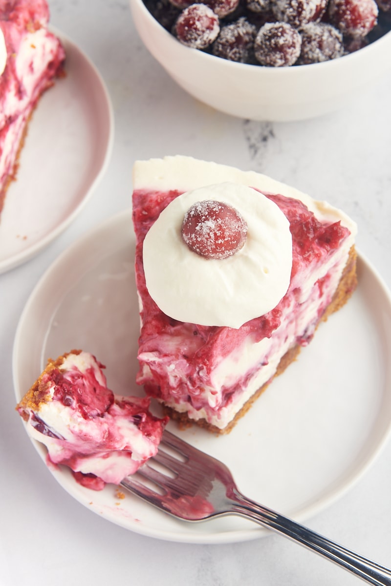 a slice of no-bake cranberry cheesecake with a bite on a fork on a white plate