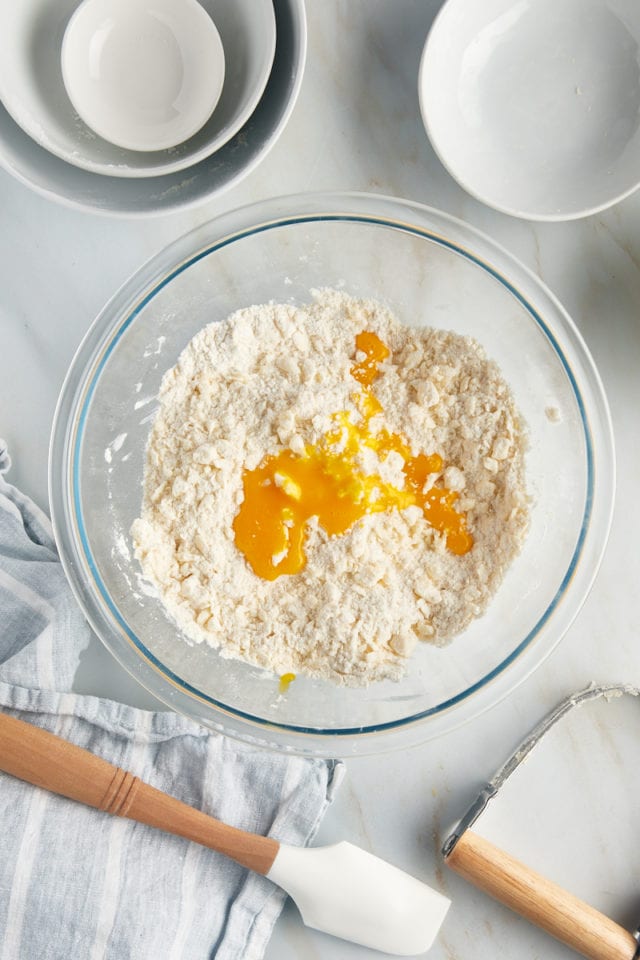 Overhead view of egg yolk added to ingredients for tart dough in bowl