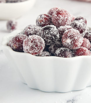 sugared cranberries in a white bowl with more berries in the foreground and background