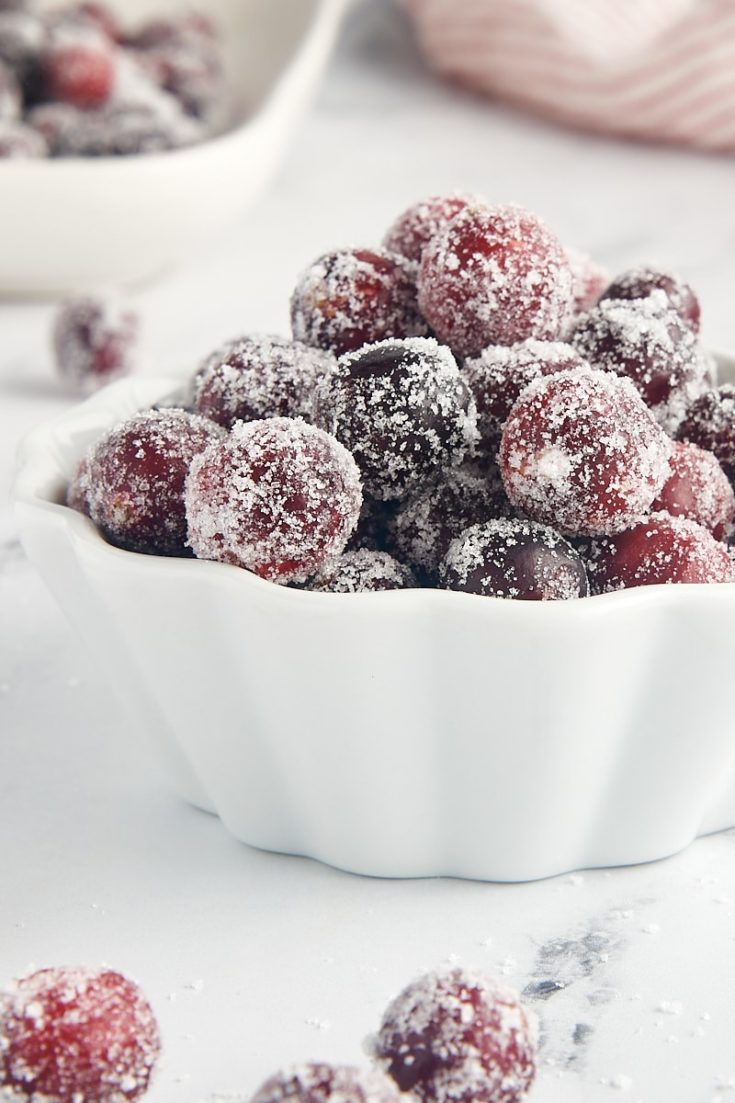 sugared cranberries in a white bowl with more berries in the foreground and background