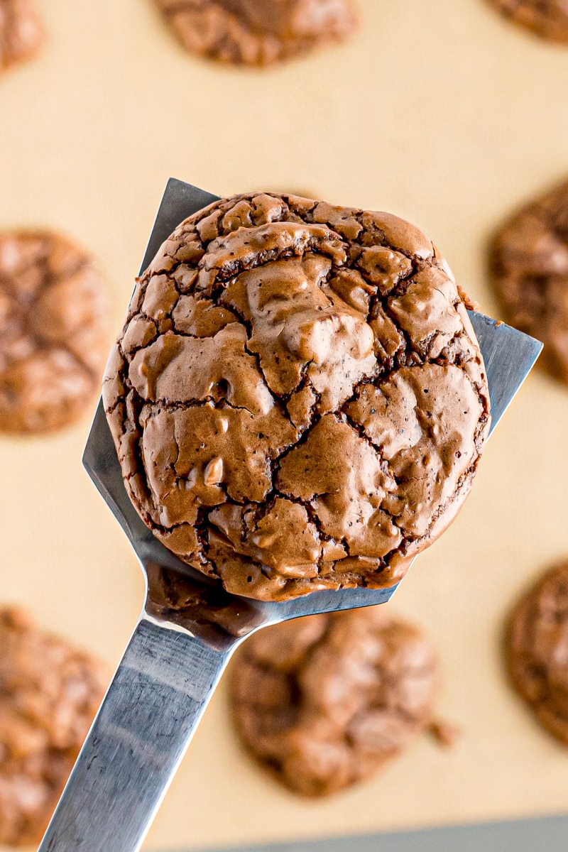 Spatula holding outrageous chocolate cookie over parchment-lined pan
