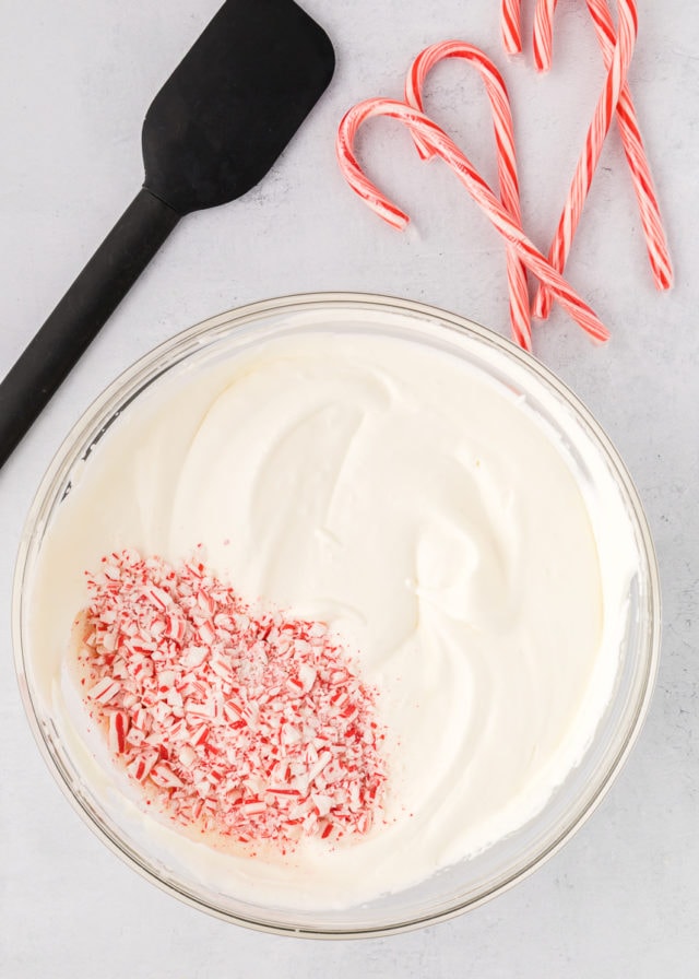 overhead view of candy cane pieces added to peppermint ice cream in a glass mixing bowl