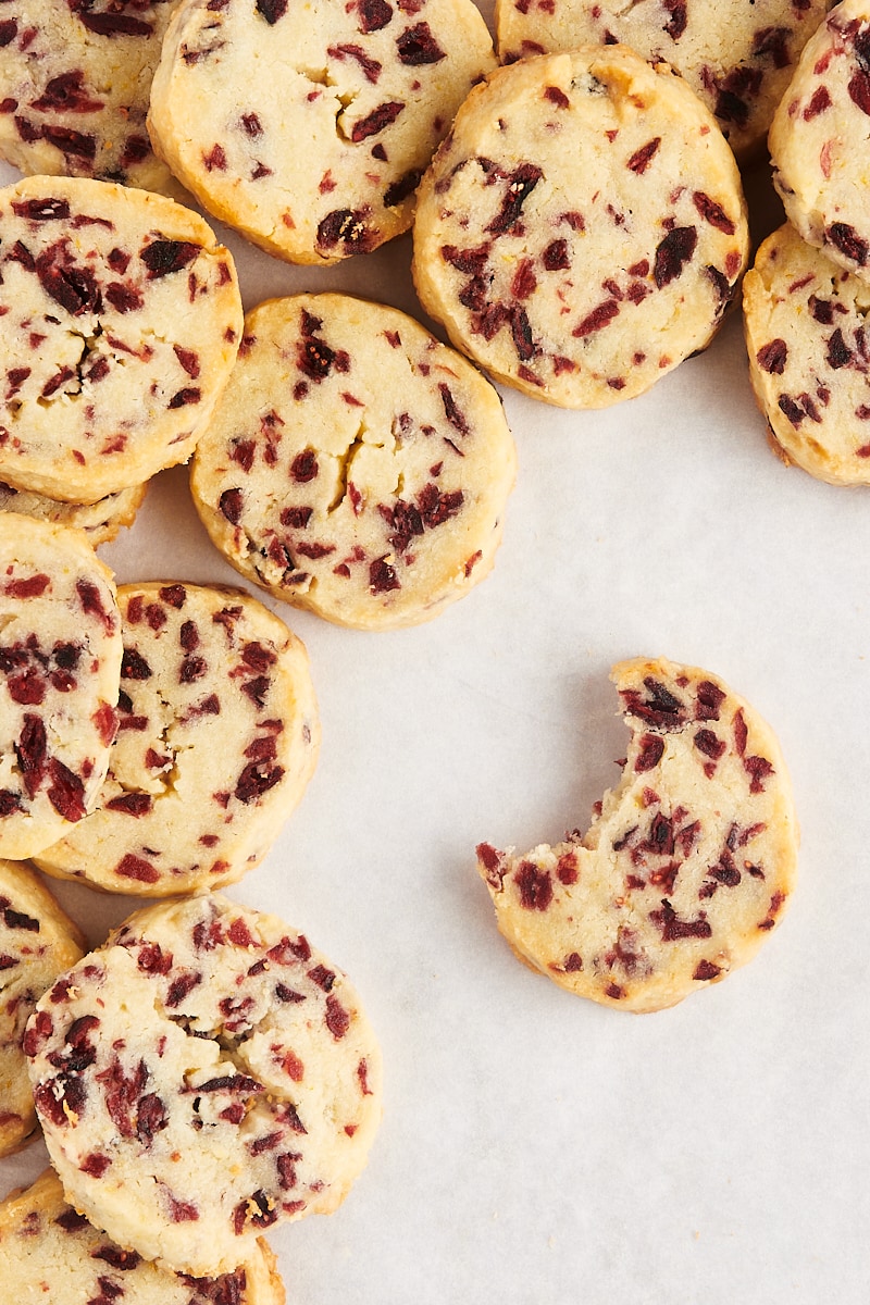 Pile of cranberry orange shortbread cookies with a bitten cookie set off to the side