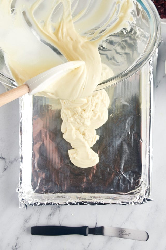 overhead view of melted white chocolate being poured onto a foil-lined baking sheet