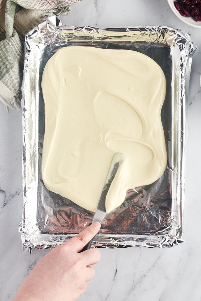 overhead view of melted white chocolate being spread on a foil-lined baking sheet