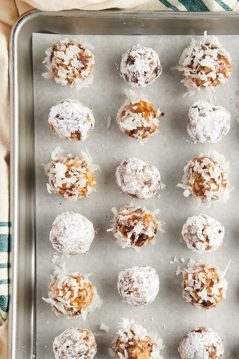 Overhead view of date balls coated in coconut and powdered sugar setting on sheet pan