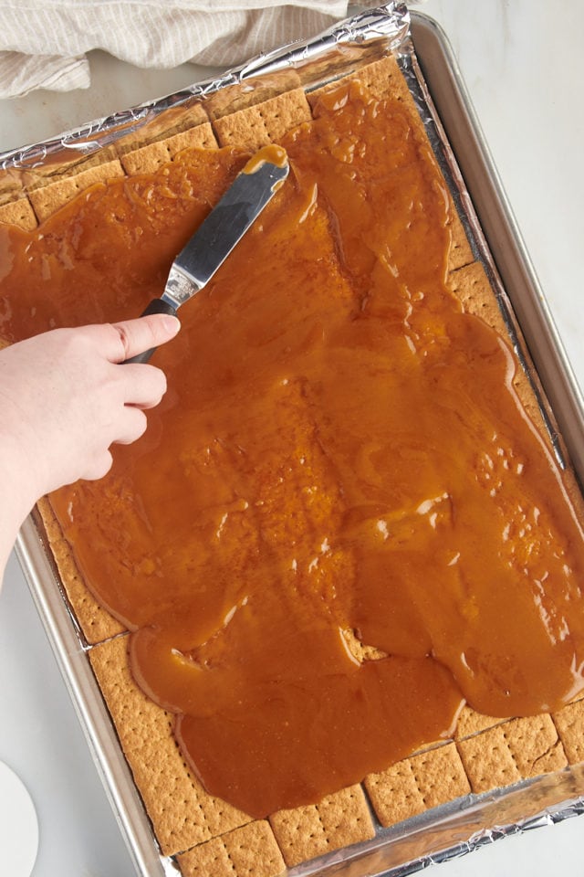 overhead view of caramel being spread over graham crackers in a half sheet pan