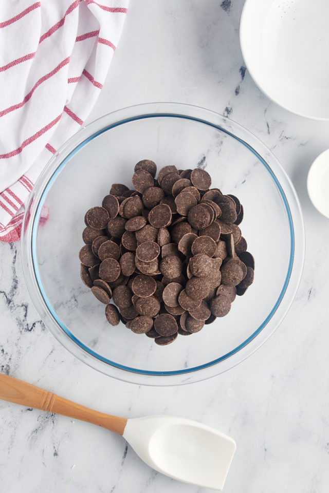 overhead view of dark chocolate discs in a glass mixing bowl