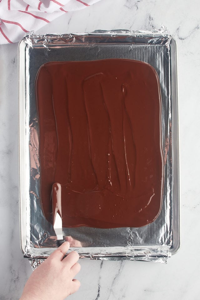 overhead view of melted chocolate being spread on a foil-lined baking pan