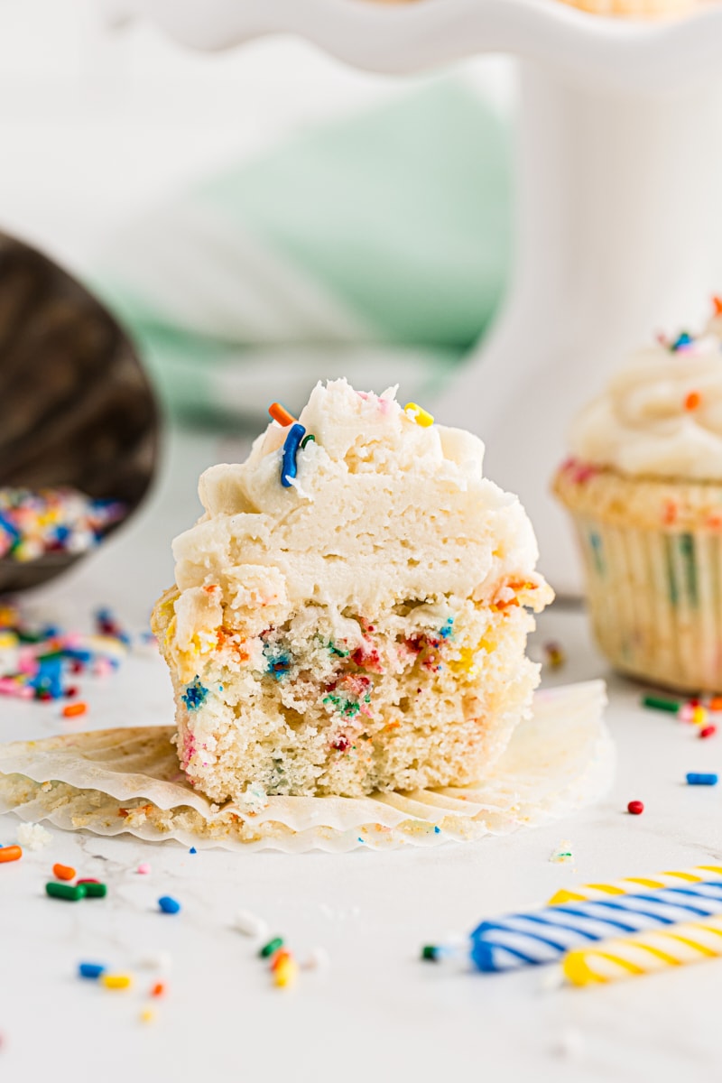 half of a confetti cupcake with another cupcake and sprinkles in the background