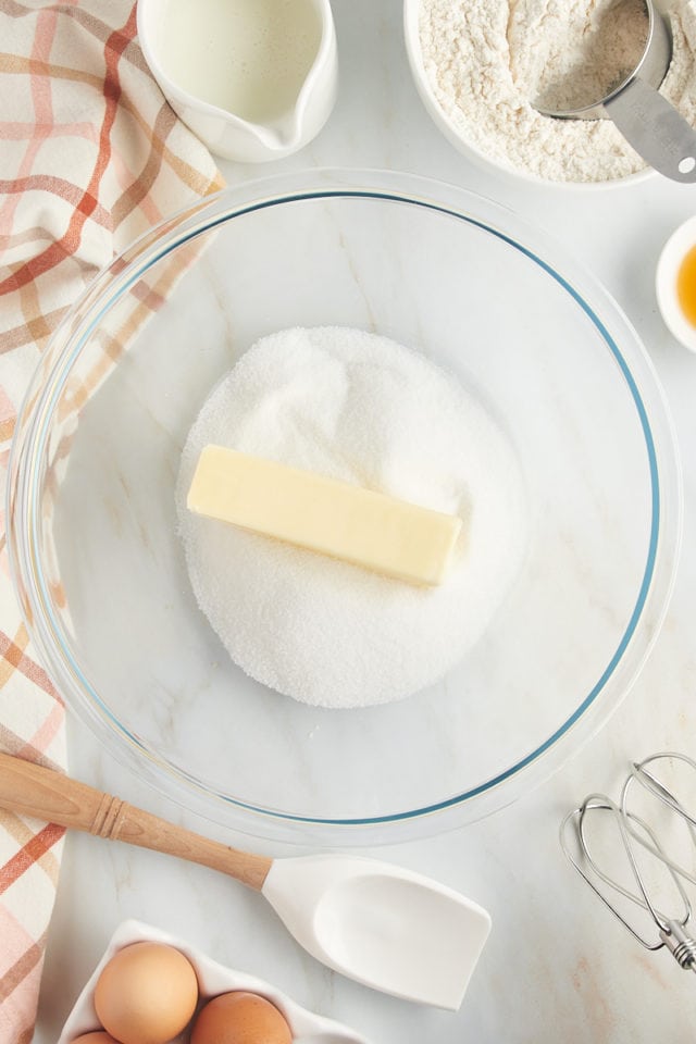 Overhead view of stick of butter added to bowl of sugar