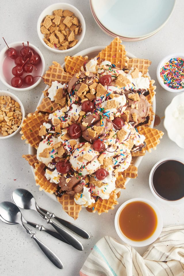 overhead view of assembled ice cream nachos surrounded by bowls of toppings, plates, and spoons