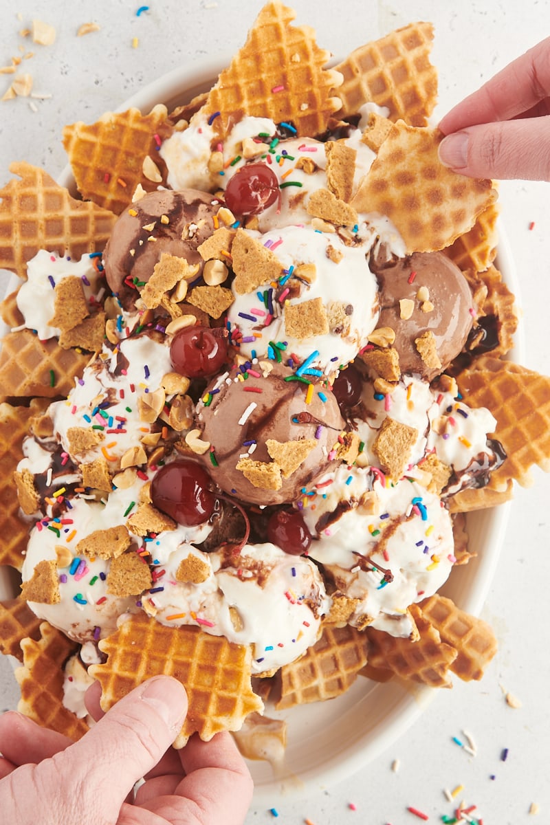 ice cream nachos on a large white plate with two hands reaching in to grab a bite