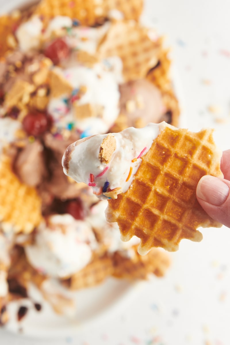 a hand holding a waffle cone chip with ice cream and toppings