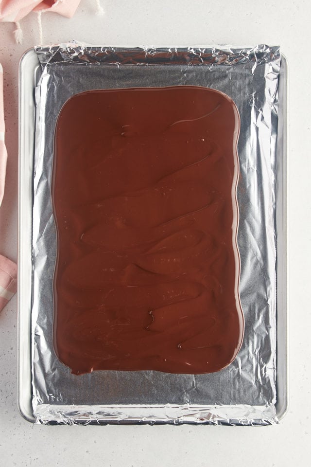 overhead view of melted dark chocolate spread on a foil-lined half sheet pan