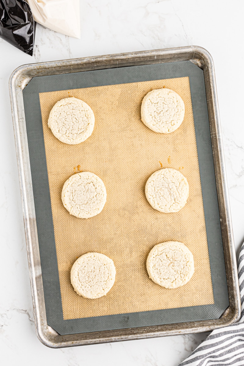 A single freshly baked black and white cookie with lightly browned edges on a lined baking sheet.