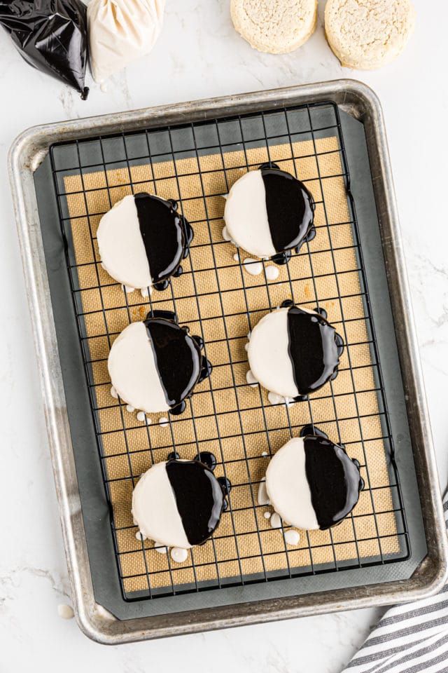 overhead view of freshly iced black and white cookies on a wire rack set over a baking sheet