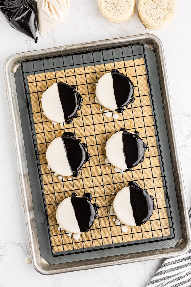 Freshly iced black and white cookies with both vanilla and chocolate frosting, on a wire rack.